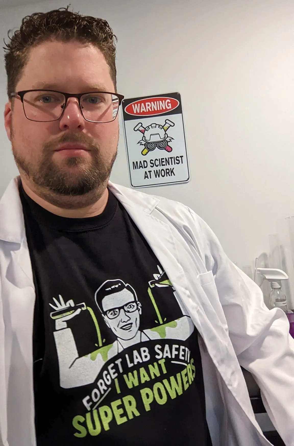 Me with a t-shirt that says 'forget lab safety, I want superpowers'. On the wall is a sign saying 'mad scientist at work'