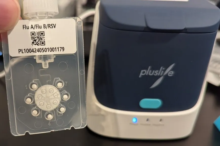 A Pluslife test card with 7 wells, a pluslife machine in the background